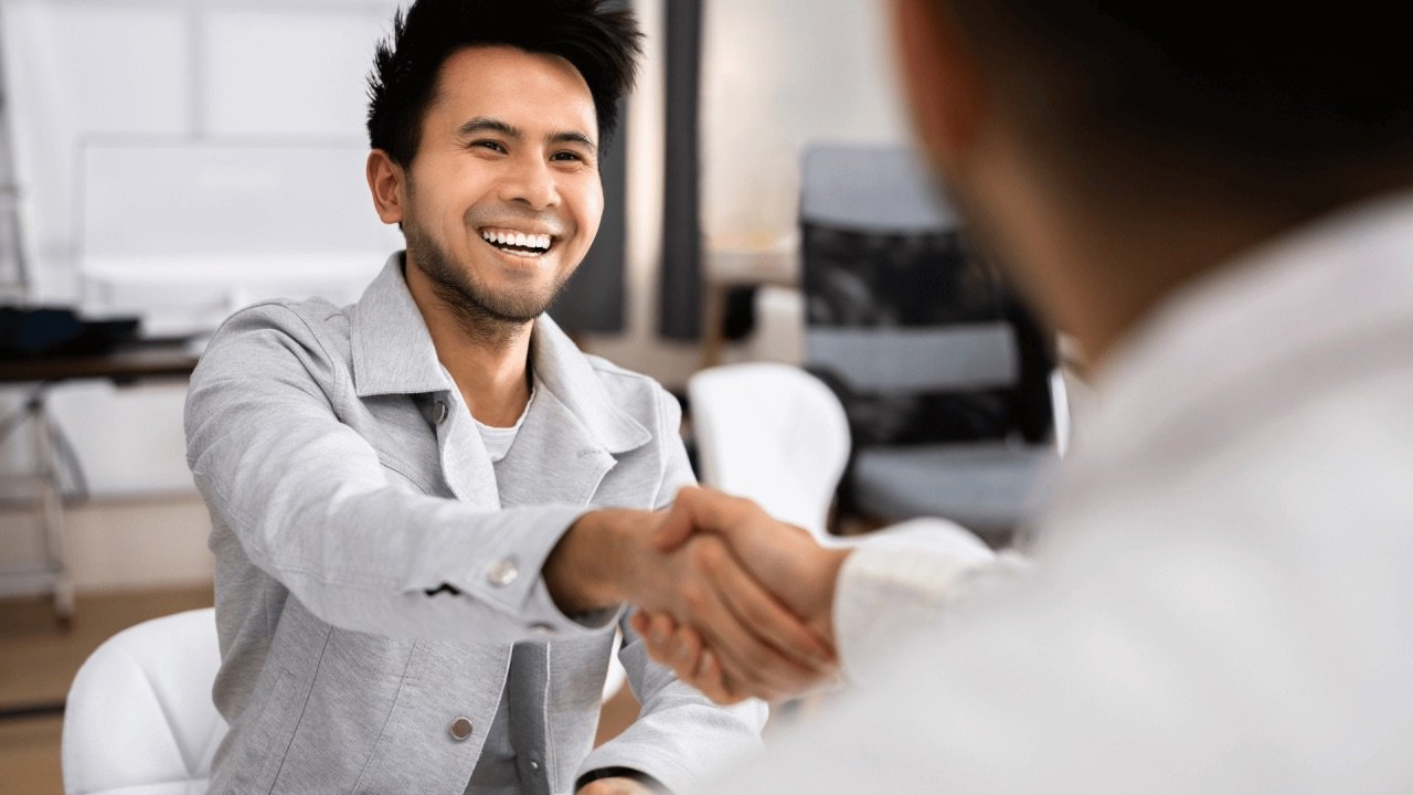 An employer shaking hands with a new team member across an office desk