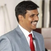 Dr. Ramanujam smiling in a grey suit and red tie